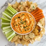 Buffalo chicken dip with tortilla chips, carrots, celery, and baguette slices arranged on a platter.